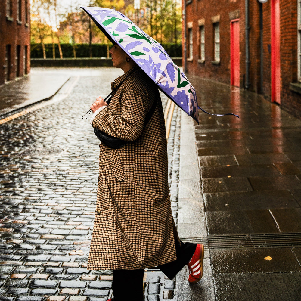 Person holding a floral umbrella on a rainy street with brick buildings.