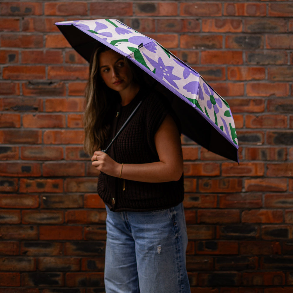 Person holding a floral-patterned umbrella against a brick wall