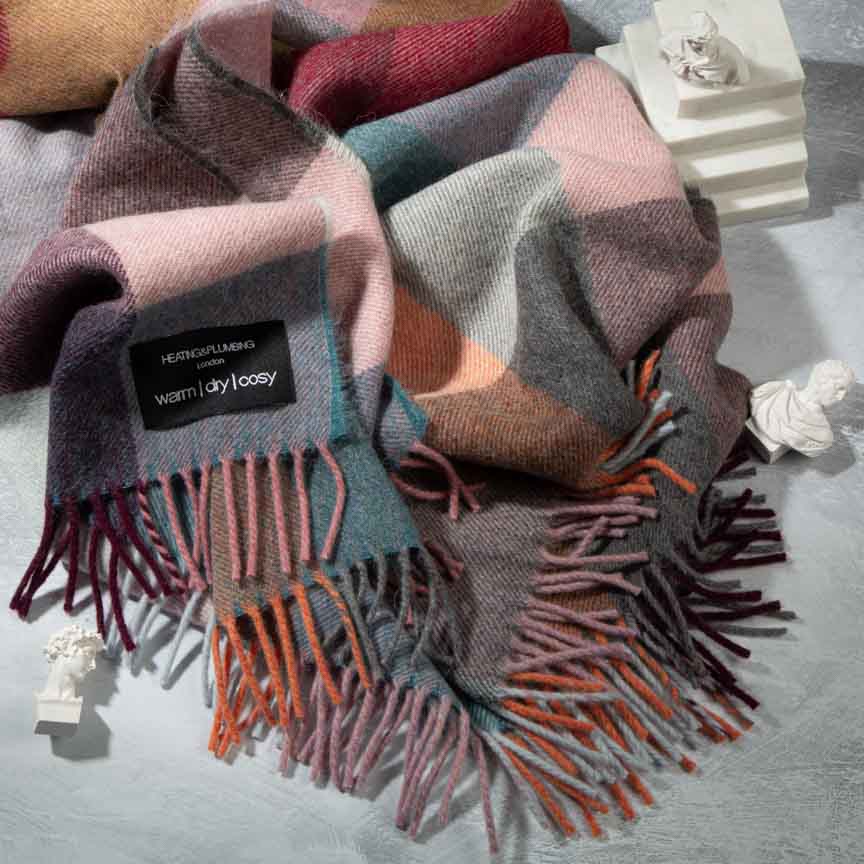 Colourful plaid blanket with fringes on a grey surface, featuring a brand label.