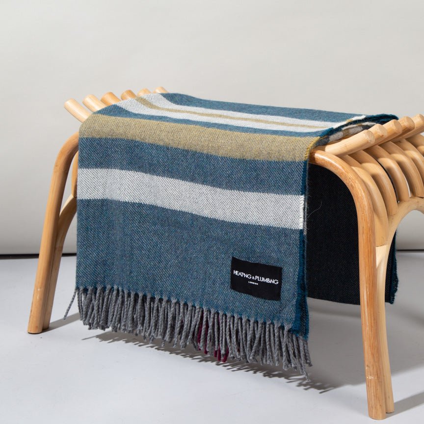 Striped alpaca merino blanket draped over a wooden chair on a light gray background