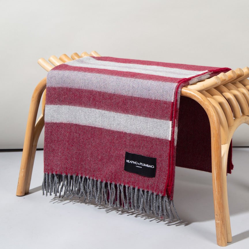 Red and grey striped alpaca blanket draped over a wooden stool on a light background