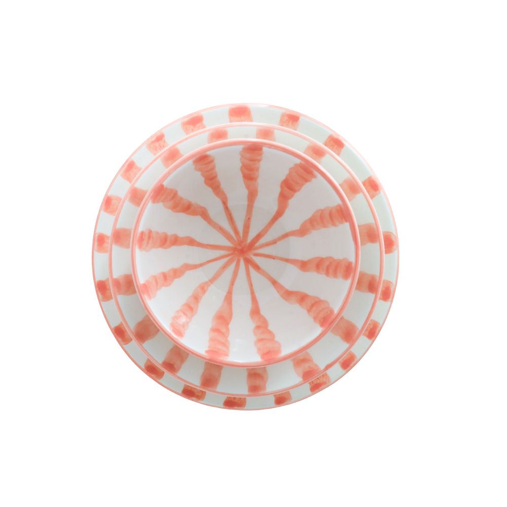 A white ceramic plate with a coral-pink radial starburst pattern in the center and matching pink stripes around the rim, shown from a top-down view on a white background.