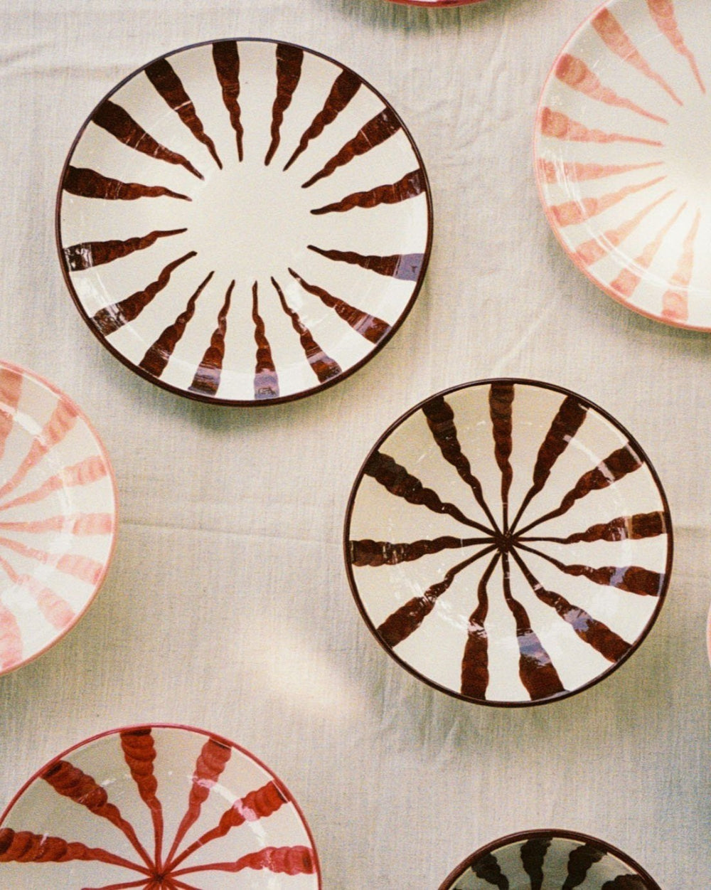 Hand-painted Woven Rosa Wave ceramic plates in brown, pink and red on a white tablecloth