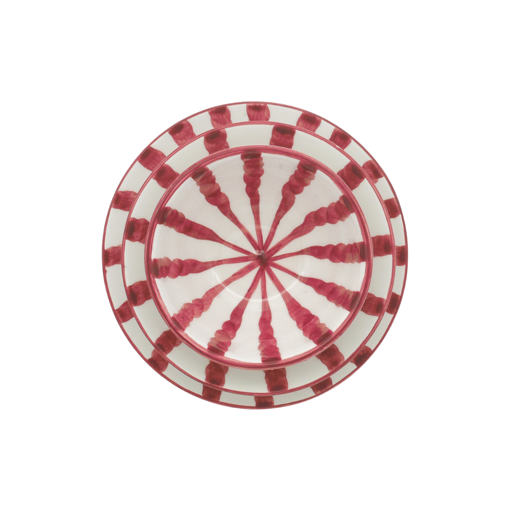 A round ceramic plate with a red and white geometric pattern, featuring radiating red stripes and checkered borders on a white background.