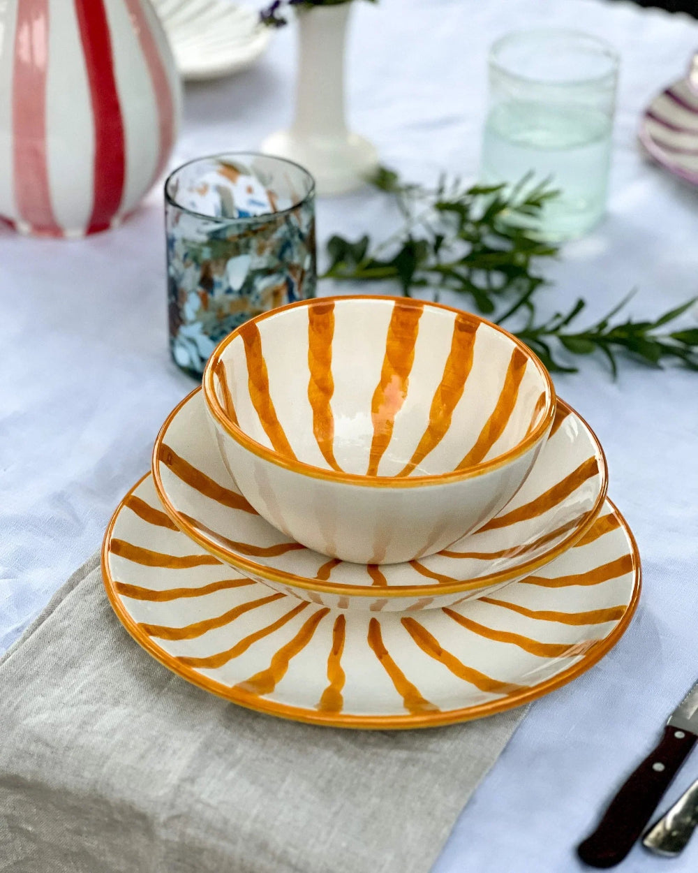 Striped ceramic bowl and saucer set on a table with a white tablecloth and decorative elements.