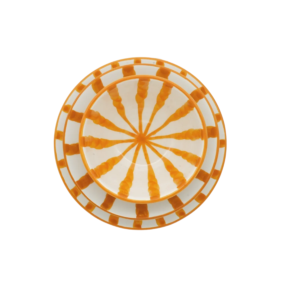 A round ceramic plate with a white base decorated with an orange sunburst pattern in the center and a matching orange and white striped border.